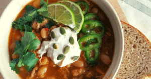 Bowl of chicken chili with sour cream cilantro jalepanos and roasted pumpkin seeds