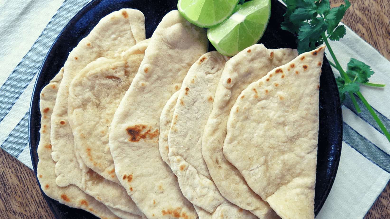 Sourdough white flour tortillas folded on a plate with lime and cilantro